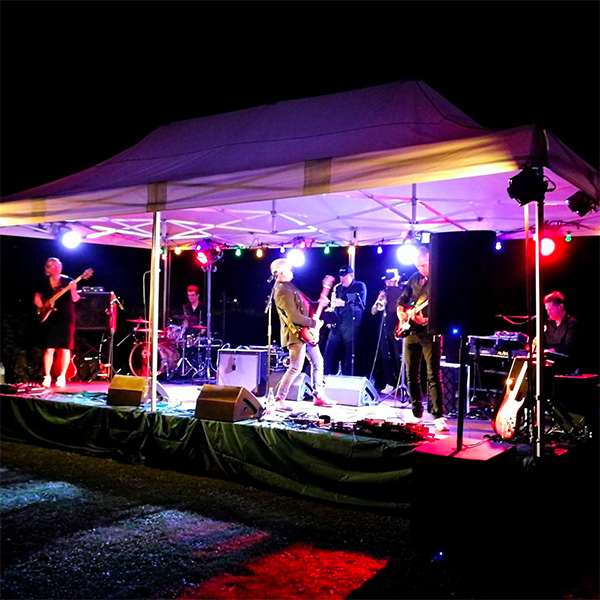 Een foto van Replay op een podium op een tuinfeest. Het is donker, verchillende kleurrijke spots maken sfeer.