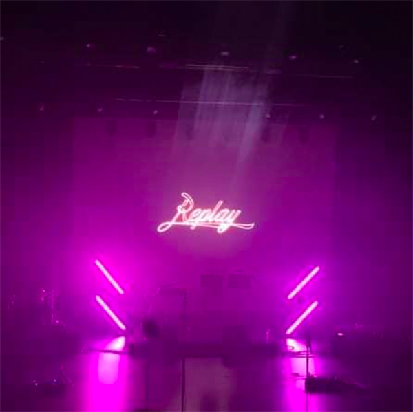 Het logo van Replay geprojecteerd op een scherm in paarse neon-gloed, net voor de start van een optreden.